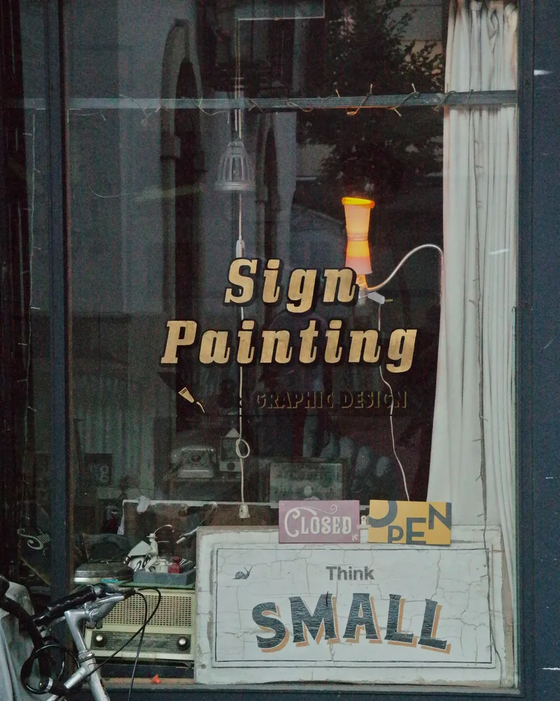 Escaparate con las palabras «Sign Painting» pintadas y doradas sobre el cristal, con rótulos pequeños apoyados en el interior